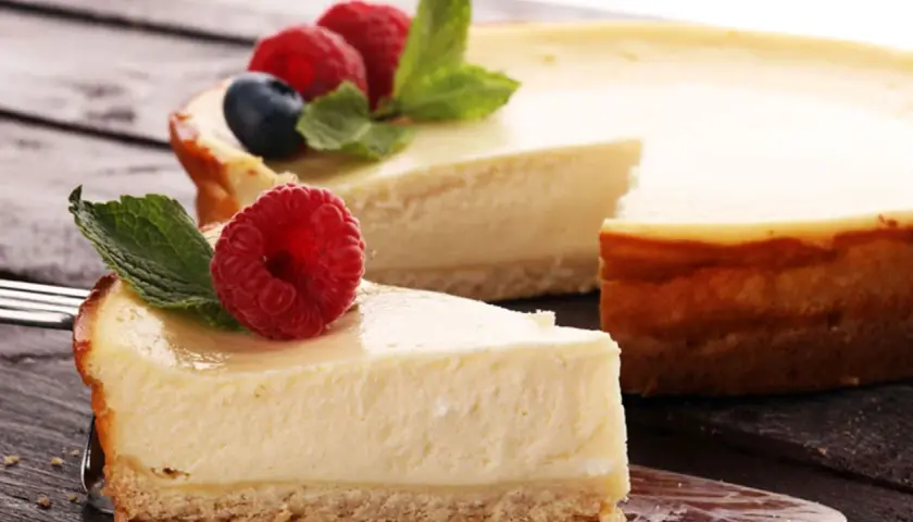 Una deliciosa tarta de queso, con una porción servida en un tenedor, decorada con frambuesas frescas y hojas de menta.