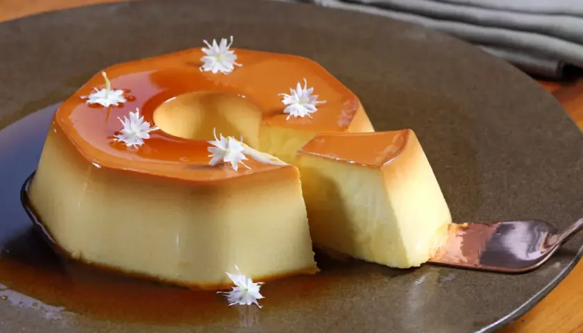 Delicioso flan de manzana con caramelo líquido y decorado con flores blancas. Una porción se sirve con una cuchara.
