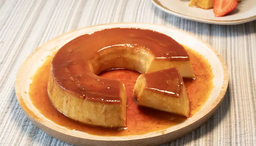 Un delicioso flan de leche condensada bañado en caramelo líquido, servido en un plato de madera.