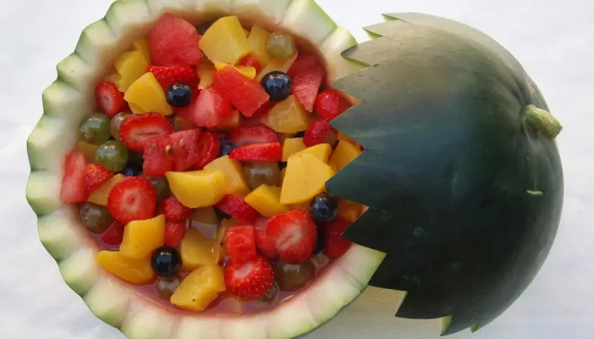Deliciosa macedonia de frutas servida en una sandía tallada, con fresas, melocotón, uvas y arándanos.