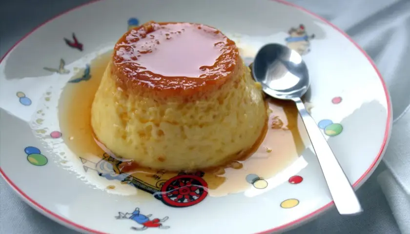 Delicioso flan de huevo casero con caramelo líquido, servido en un plato con dibujos infantiles.