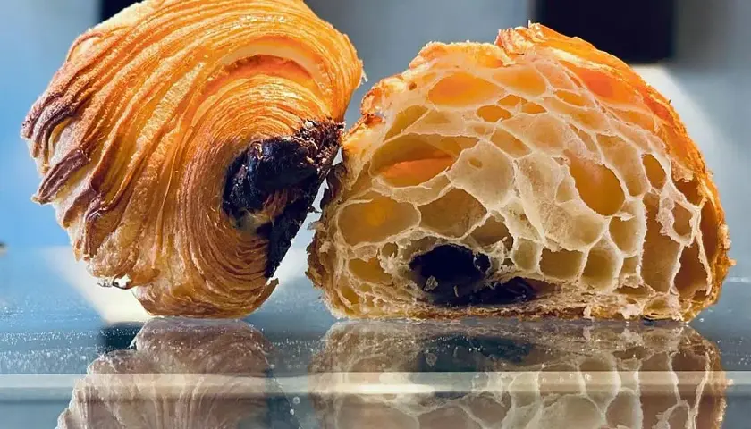 Dos mitades de un croissant de chocolate, una entera y otra cortada, revelan su interior aireado y el chocolate derretido.