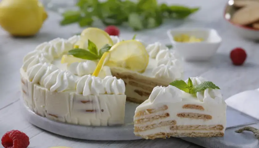 Deliciosa tarta de limón con leche condensada, decorada con crema batida, rodajas de limón y menta. Una rebanada muestra sus capas de galleta y crema.