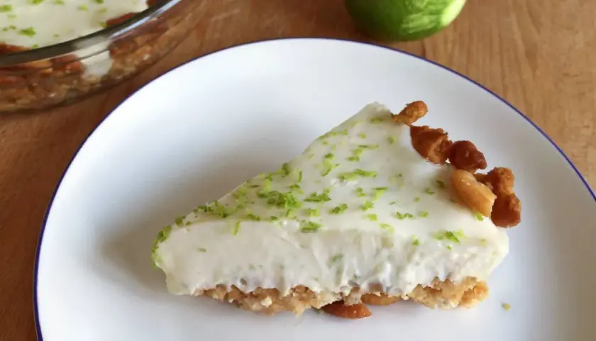 Rebanada cremosa de key lime pie, con ralladura de lima y trozos de galleta en el borde.