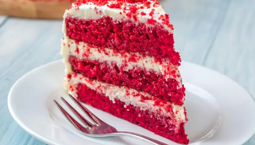 Rebanada de tarta red velvet con capas de bizcocho rojo y crema blanca, lista para disfrutar. Los ingredientes de esta tarta son un secreto delicioso.