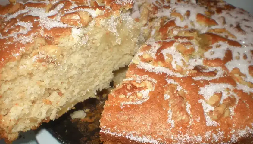 Un delicioso bizcocho de manzana y nueces, espolvoreado con azúcar, con una rebanada retirada.