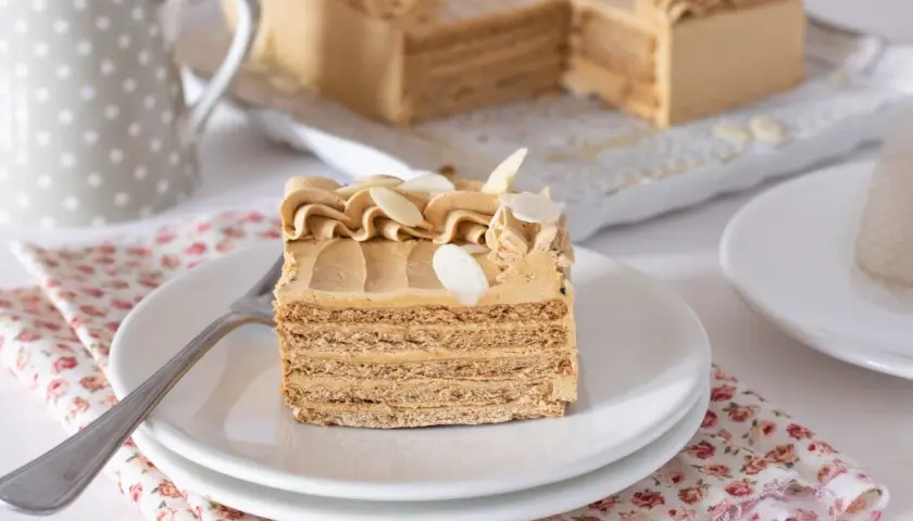 Deliciosa tarta de moka en capas, decorada con crema y almendras. Un trozo servido en plato blanco, listo para disfrutar.