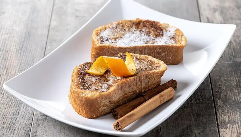 Dos deliciosas torrijas, con azúcar y canela, decoradas con piel de naranja y varas de canela. El mejor pan para torrijas, esponjoso y dorado.