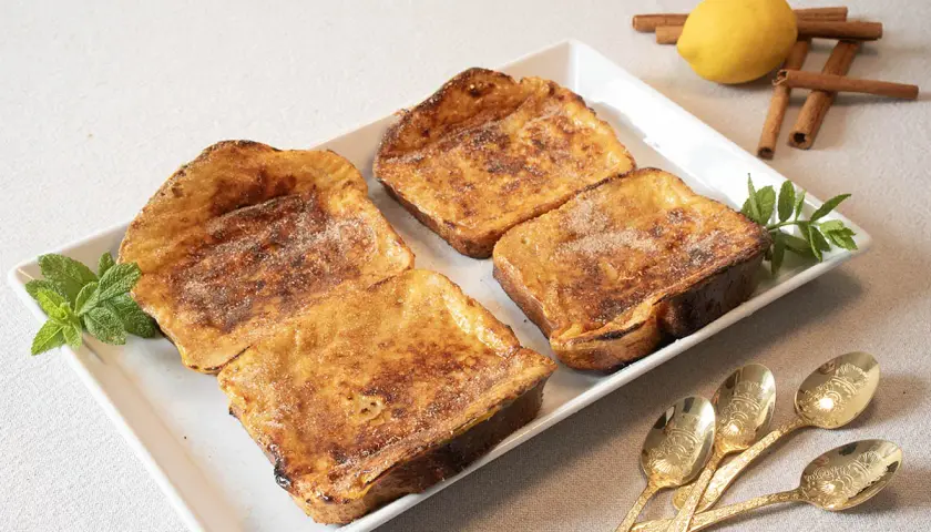 Cuatro deliciosas torrijas al horno, espolvoreadas con azúcar y canela, listas para disfrutar.