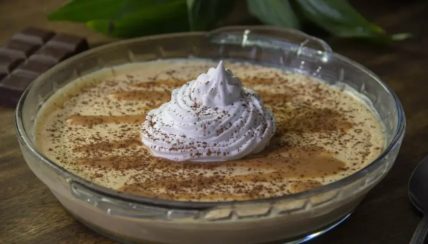 Delicioso mousse de dulce de leche en un bol de vidrio, coronado con crema batida y espolvoreado con cacao.