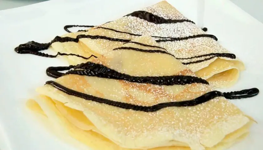 Deliciosos crepes doblados, espolvoreados con azúcar glas y cubiertos con un glaseado de chocolate. Una receta crepes perfecta para cualquier ocasión.