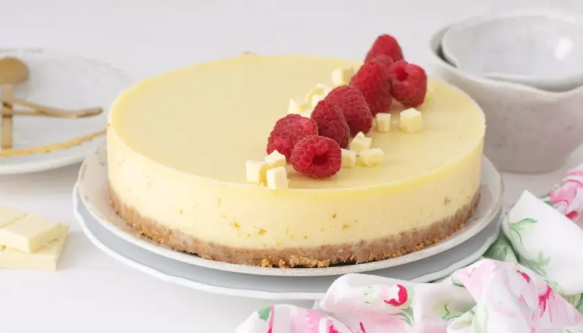 Deliciosa tarta de chocolate blanco adornada con frambuesas frescas y trocitos de chocolate.