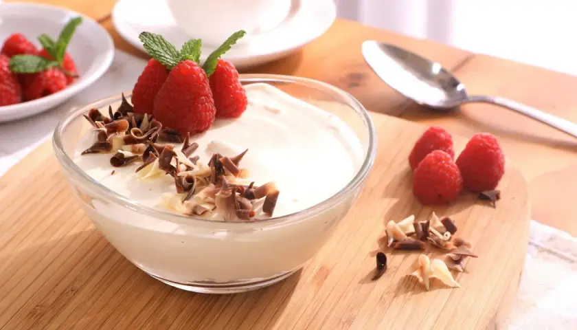 Delicioso mousse de chocolate blanco adornado con frambuesas frescas y virutas de chocolate.