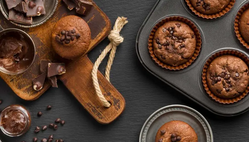 Deliciosos muffins de chocolate recién horneados, algunos en molde y otros listos para disfrutar, acompañados de trozos de chocolate y crema.