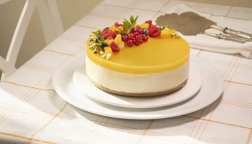 Deliciosa tarta de mango y queso, cubierta con gelatina amarilla y decorada con frutos rojos y pistachos.