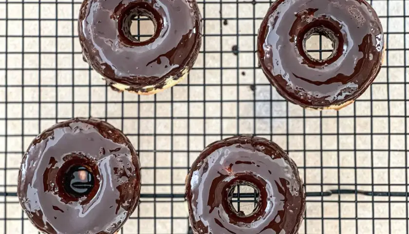 Cuatro deliciosos donuts glaseados con chocolate oscuro, listos para disfrutar. ¡Así es como hacer donuts caseros!