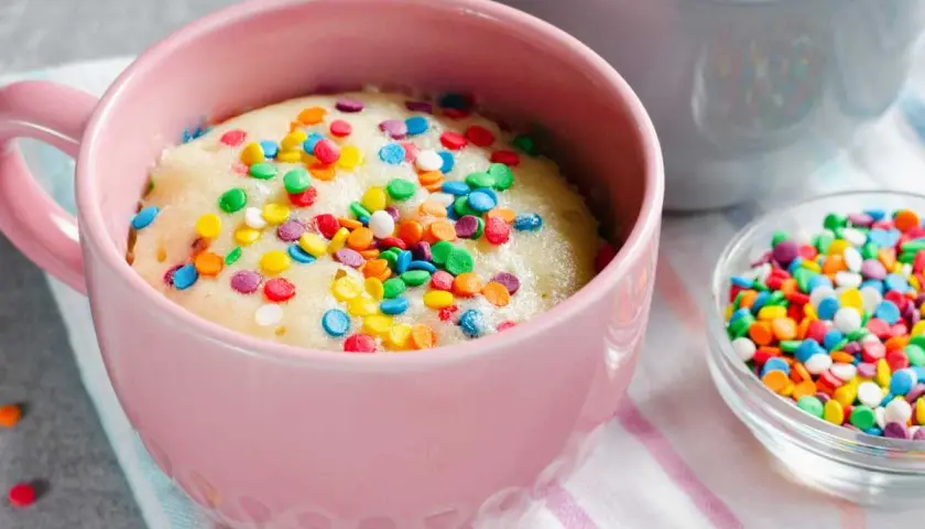 Un delicioso bizcocho al microondas en una taza rosa, cubierto de coloridas chispas. ¡Listo para disfrutar en minutos!
