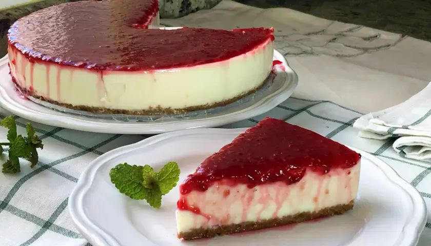 Deliciosa tarta de yogur sin horno cubierta con mermelada de frutos rojos. Un trozo servido con menta fresca.