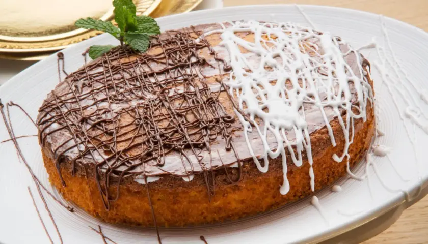 Tarta de zanahoria y coco, decorada con glaseado de chocolate y blanco, y una ramita de menta.