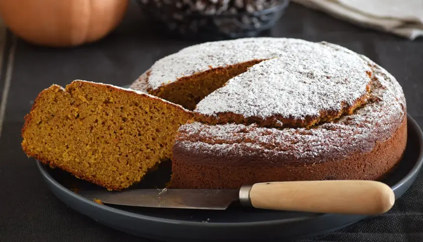 Dos rebanadas de bizcocho de calabaza apiladas, espolvoreadas con azúcar glas, con menta y tenedor.