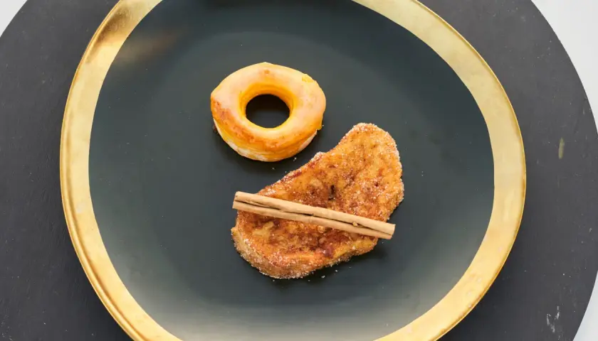 Rosquillas de Alcalá y torrija con canela, servidas en plato negro con borde dorado.