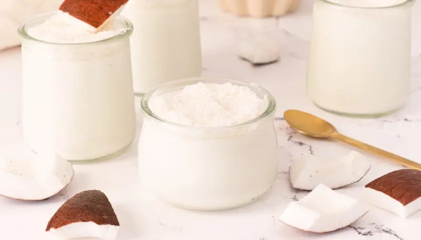 Delicioso mousse de coco en vasitos de cristal, decorado con coco rallado y trozos de coco fresco.