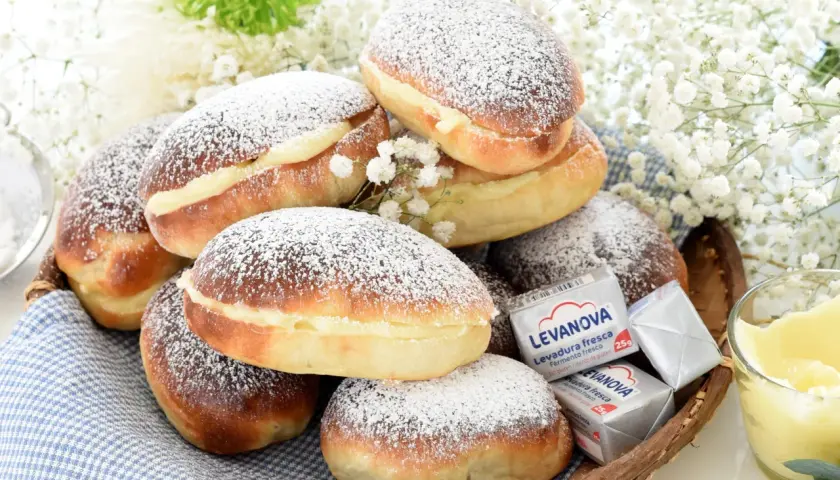 Bollos de mantequilla cubiertos de azúcar glas, rellenos de crema, junto a levadura y flores blancas.