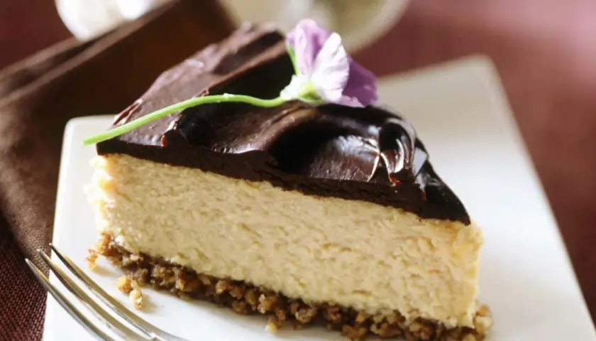 Deliciosa tarta de queso y chocolate, con una capa cremosa y cobertura brillante, decorada con una flor.
