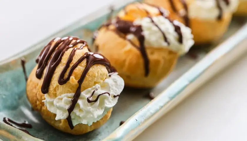 Profiteroles rellenos de crema y bañados en chocolate, perfectos para tu próxima receta.