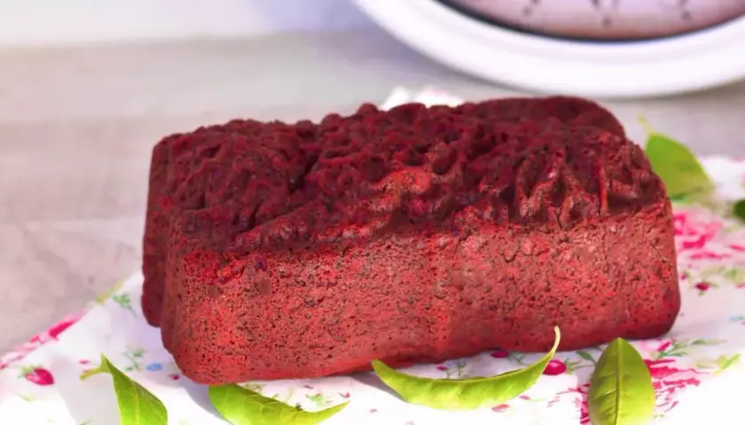 Un delicioso pan de red velvet, con una textura esponjosa y un color vibrante, decorado con hojas verdes sobre un mantel floral.