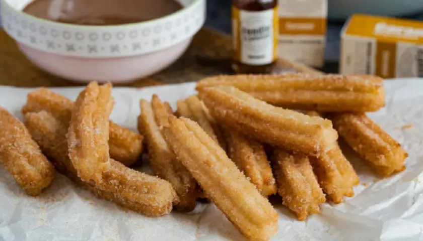 Montón de churros caseros recién hechos, espolvoreados con azúcar y canela, listos para mojar en chocolate caliente.