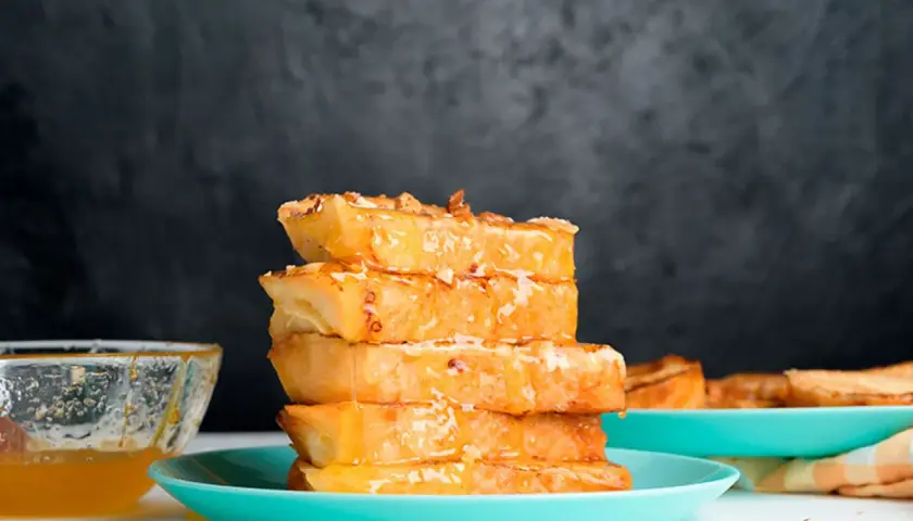 Torrijas de horchata doradas y jugosas, apiladas y bañadas en miel, con un cuenco de miel al lado.