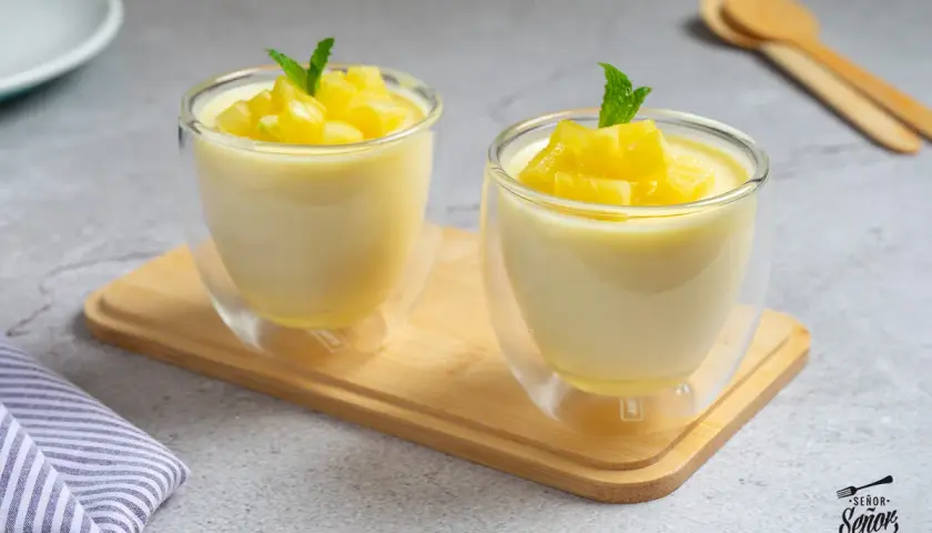 Dos copas de cristal con un delicioso mousse de piña, decoradas con trocitos de piña y menta.