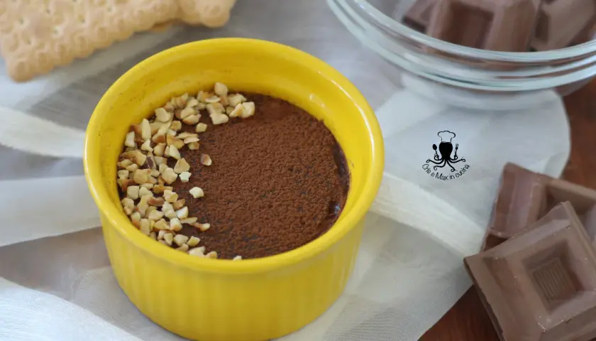 Pudín de chocolate cremoso en un cuenco amarillo, espolvoreado con cacao y nueces picadas.