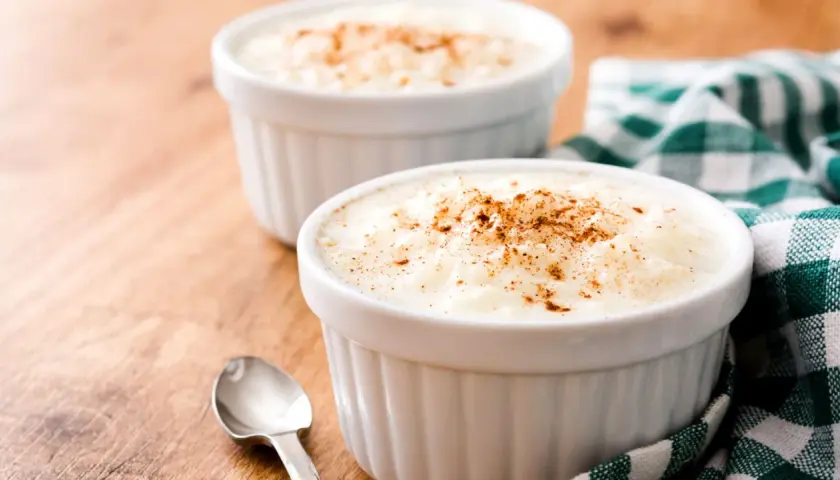 Dos ramequines de arroz con leche en microondas, espolvoreados con canela, sobre una mesa de madera.