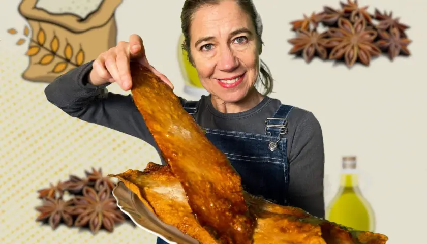 Mujer sonriente muestra una coca de vidre dorada y crujiente, con ingredientes como harina, anís estrellado y aceite de oliva de fondo.