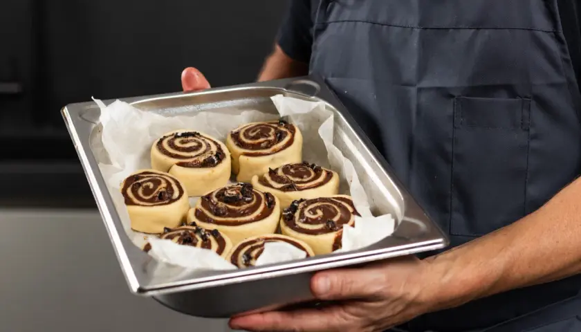 Manos sostienen una bandeja con deliciosos rollitos de canela listos para hornear.