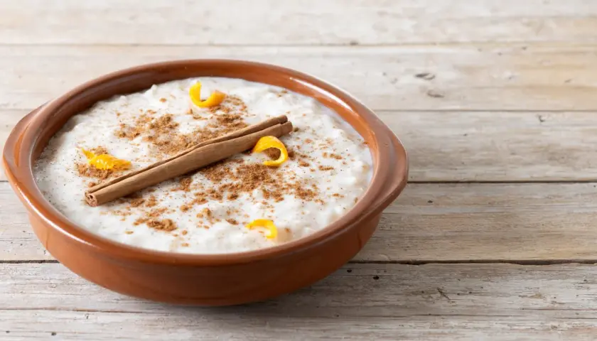 Un tazón de arroz con leche cremoso, espolvoreado con canela y adornado con cáscara de naranja y una rama de canela. ¡Perfecto para tu receta de arroz con leche cremoso!