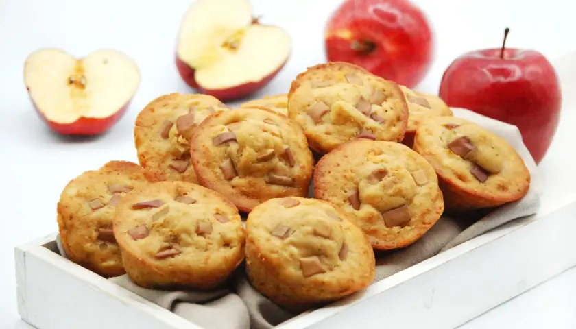 Deliciosas magdalenas de manzana, recién horneadas y listas para disfrutar. Dos manzanas rojas enteras y dos cortadas a la mitad acompañan esta tentación.