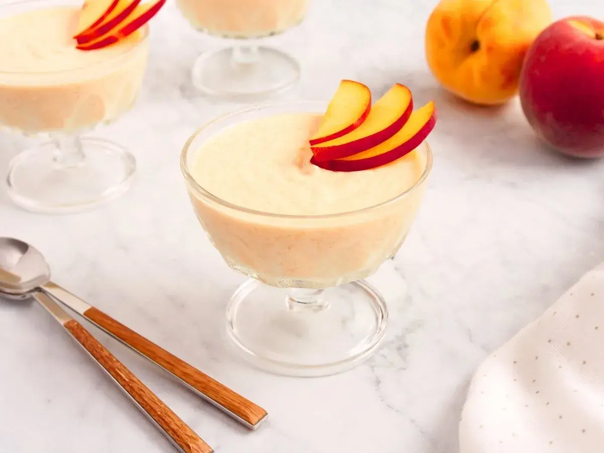 Delicioso mousse de melocotón en copas de cristal, decorado con finas láminas de melocotón.