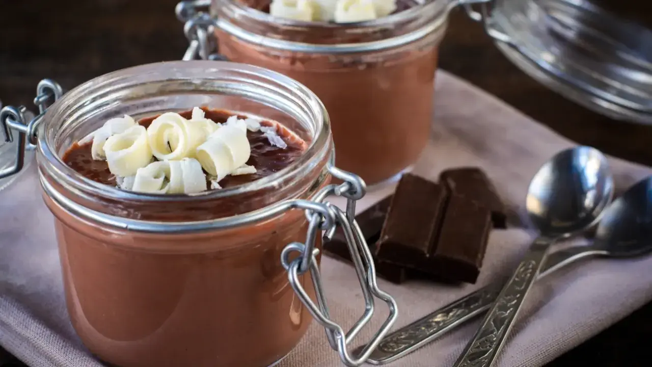 Deliciosa panna cotta de chocolate en frascos, decorada con rizos de chocolate blanco. Dos porciones listas para disfrutar.
