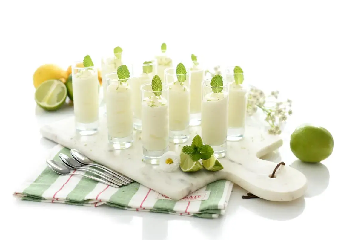 Delicioso mousse de limón en vasitos, decorado con menta y ralladura de limón. Frescura y sabor en cada bocado.