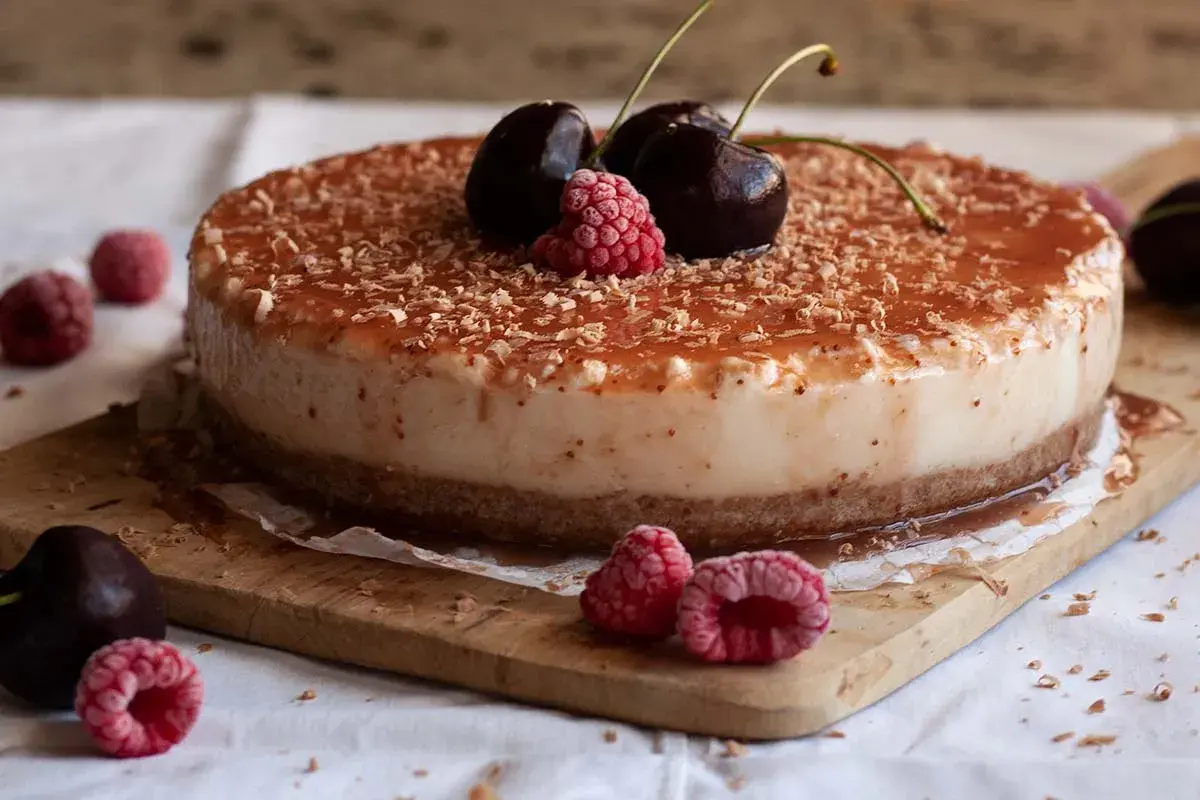 Tarta de queso con leche condensada, cubierta de mermelada y virutas de chocolate, decorada con cerezas y frambuesas.