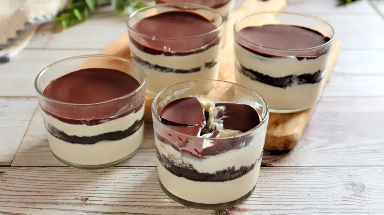 Cuatro vasitos de tiramisú de oreo, con capas de crema y galleta, cubiertos de chocolate.