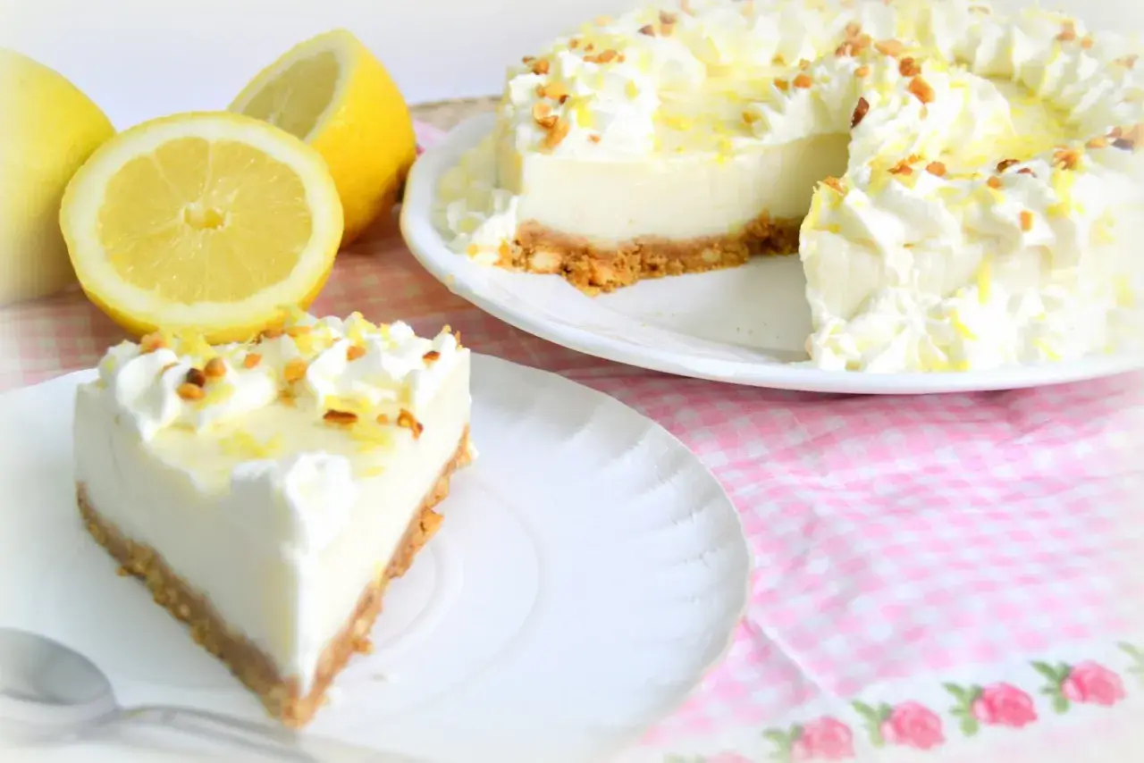 Deliciosa tarta de limón con cuajada y leche condensada, decorada con nata y ralladura de limón.