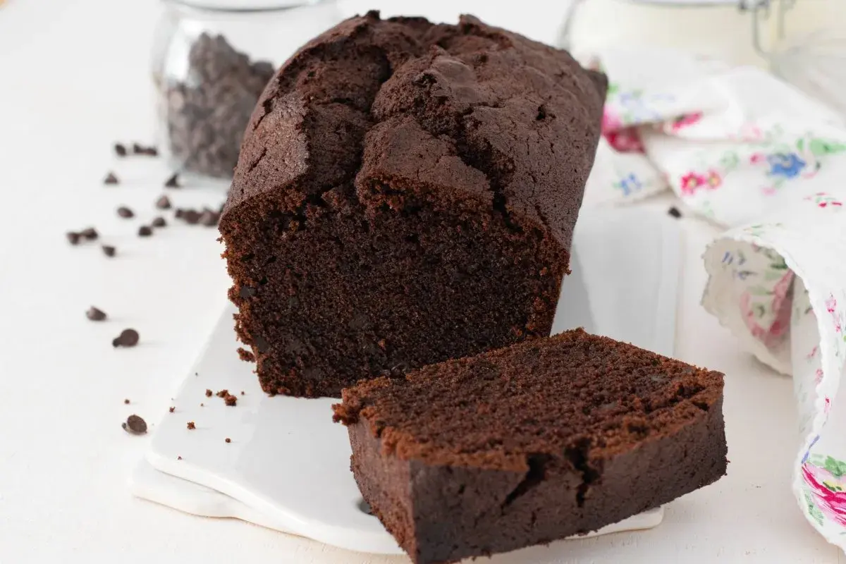 Un delicioso plum cake de chocolate, con una rebanada separada y chispas de chocolate esparcidas.