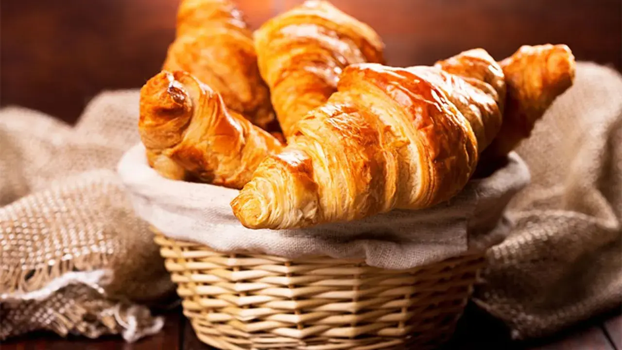 Cesta de mimbre llena de deliciosos croissants caseros, dorados y crujientes, listos para disfrutar.