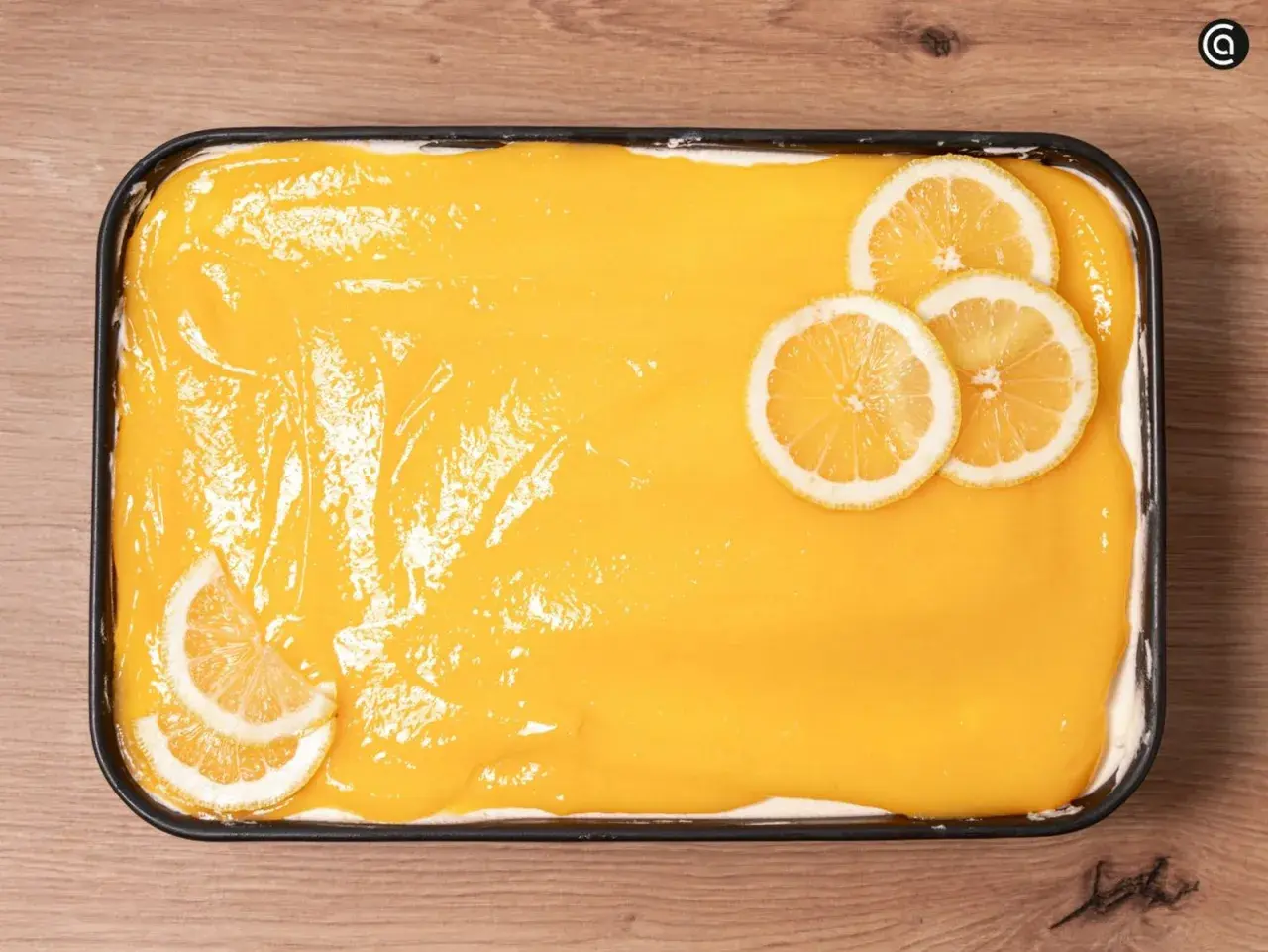 Un delicioso tiramisú de limón, cubierto con una crema amarilla brillante y decorado con rodajas de limón fresco.