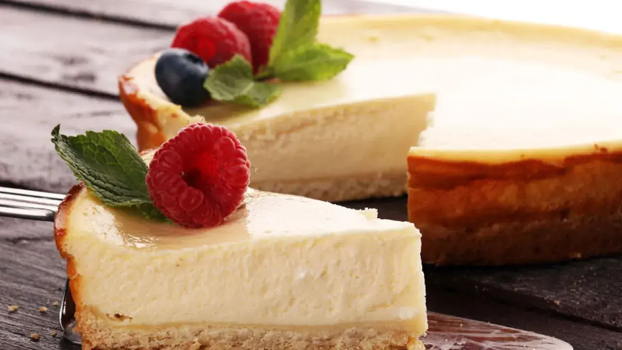 Una deliciosa tarta de queso, con una porción servida en un tenedor, decorada con frambuesas frescas y hojas de menta.