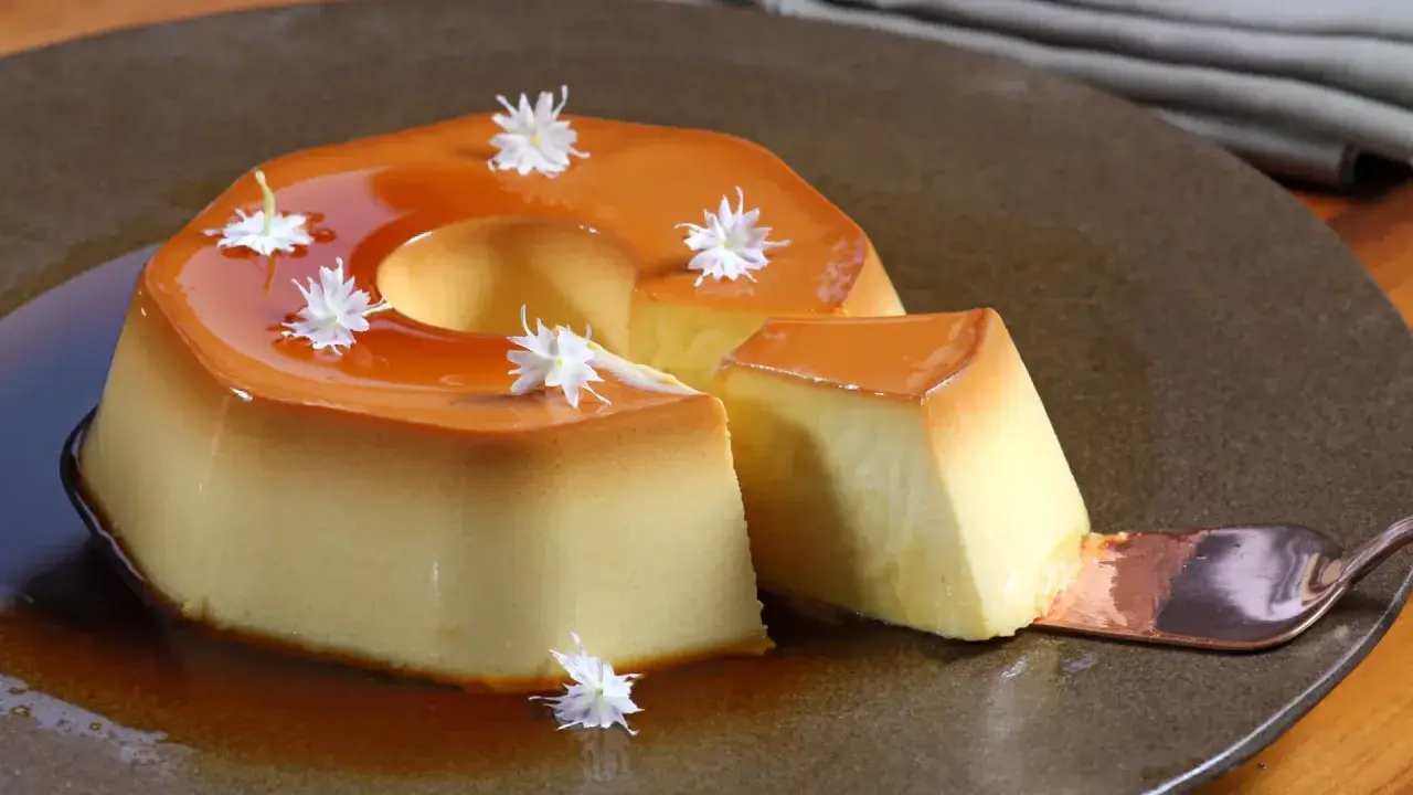 Delicioso flan de manzana con caramelo líquido y decorado con flores blancas. Una porción se sirve con una cuchara.